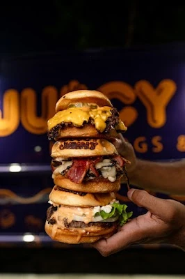 A towering stack of Juicy Joint burgers held in front of the branded counter